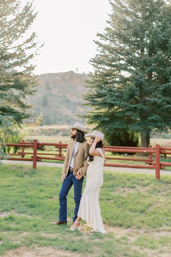 Couple in cowboy hats by a red rail fence